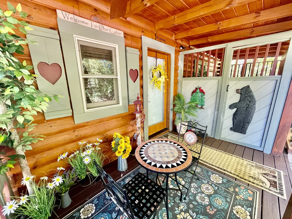 This image features a decorative table positioned by a bear motif door, with welcoming flowers and a prominent 'welcome' sign. Soft natural light suggests a porch or an entry area that bridges the indoors and the outdoors, inviting guests to set out for adventure or return to comfort.