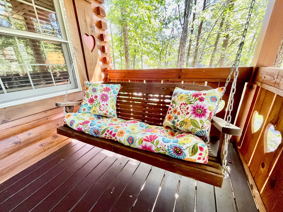 A serene view of a wooden swing seat adorned with colorful cushions, set within a charming wooden structure that invites guests to relax, read, or simply enjoy the sounds of nature.