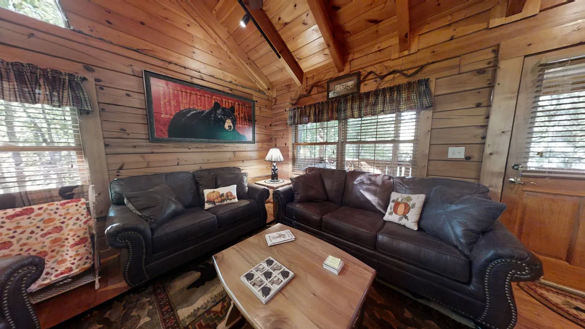 This image presents another angle of the living space with leather sofas, a coffee table, wall art, and large windows letting in soft natural light. The arrangement encourages intimate conversation or shared activities like board games, aligning with the idea of spending quality time with loved ones.
